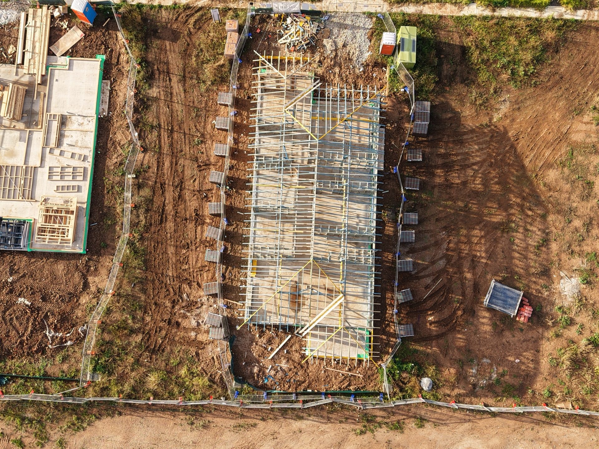 Top-down aerial of a long rectangular timber-framed structure ready for roofing